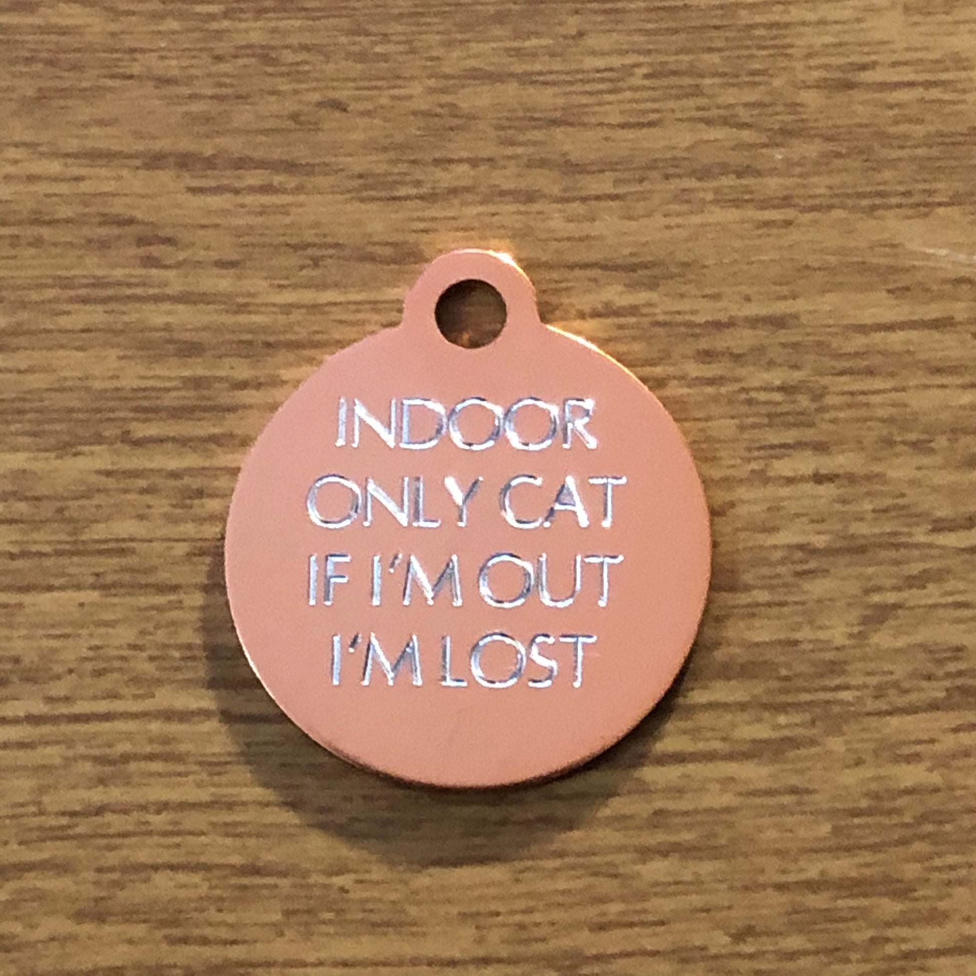 Small rose gold circle tag that says: Indoor only cat If I&#39;m out I&#39;m lost. All engraved in capital letters.