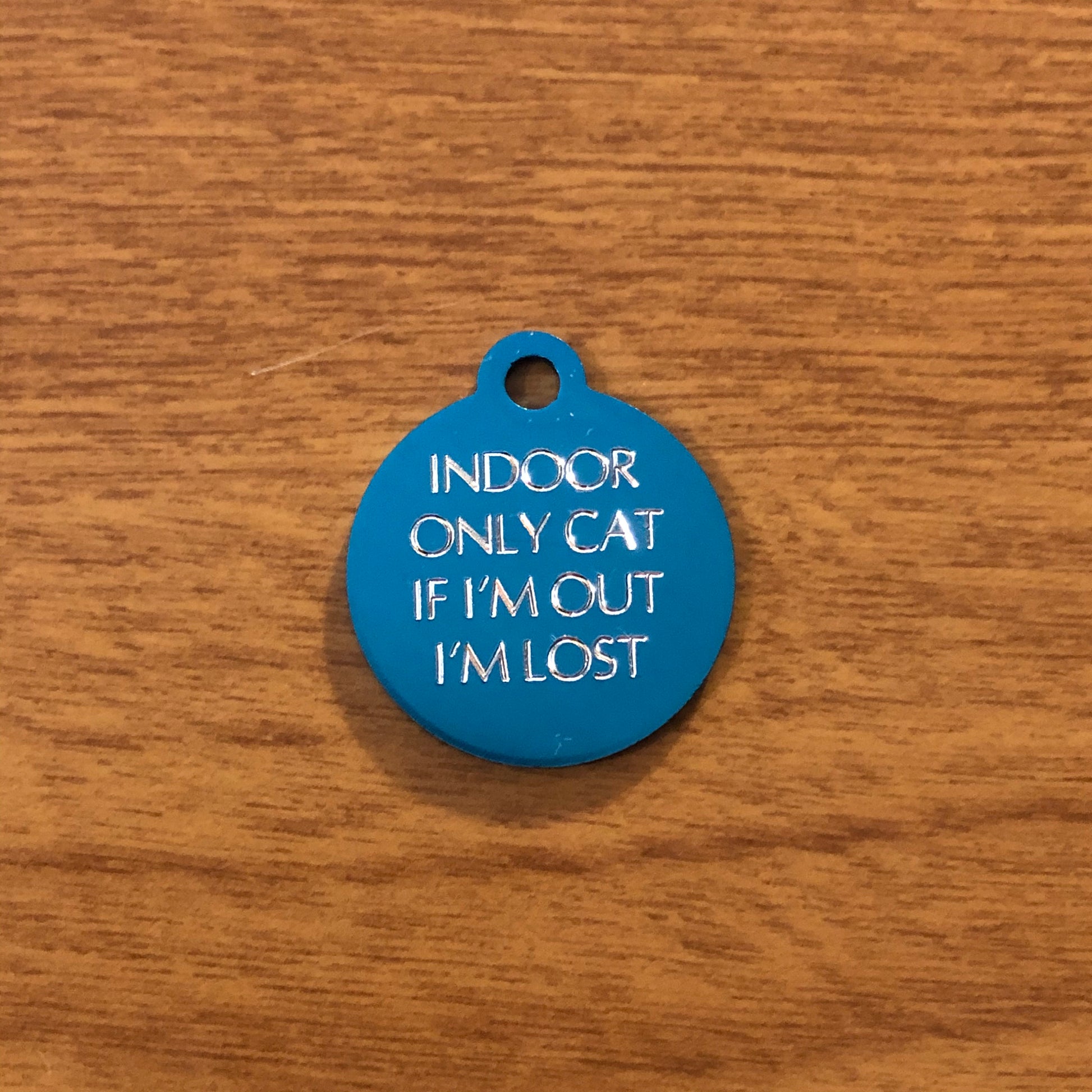 Small turquoise circle tag that says: Indoor only cat If I&#39;m out I&#39;m lost. All engraved in capital letters.