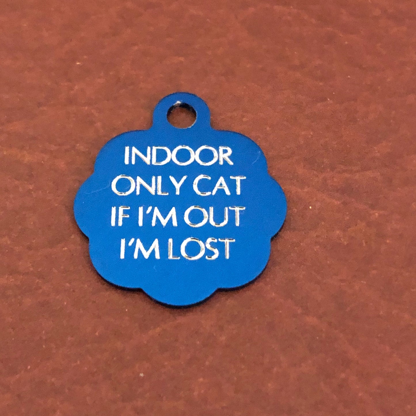 Small blue rosette tag that says: Indoor only cat If I&#39;m out I&#39;m lost. All engraved in capital letters.