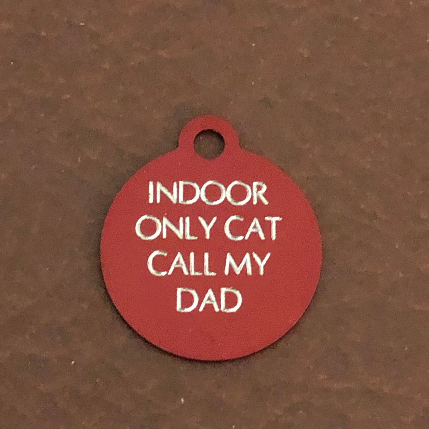 Small red circle tag that says: Indoor only cat call my dad. All engraved in capital letters.