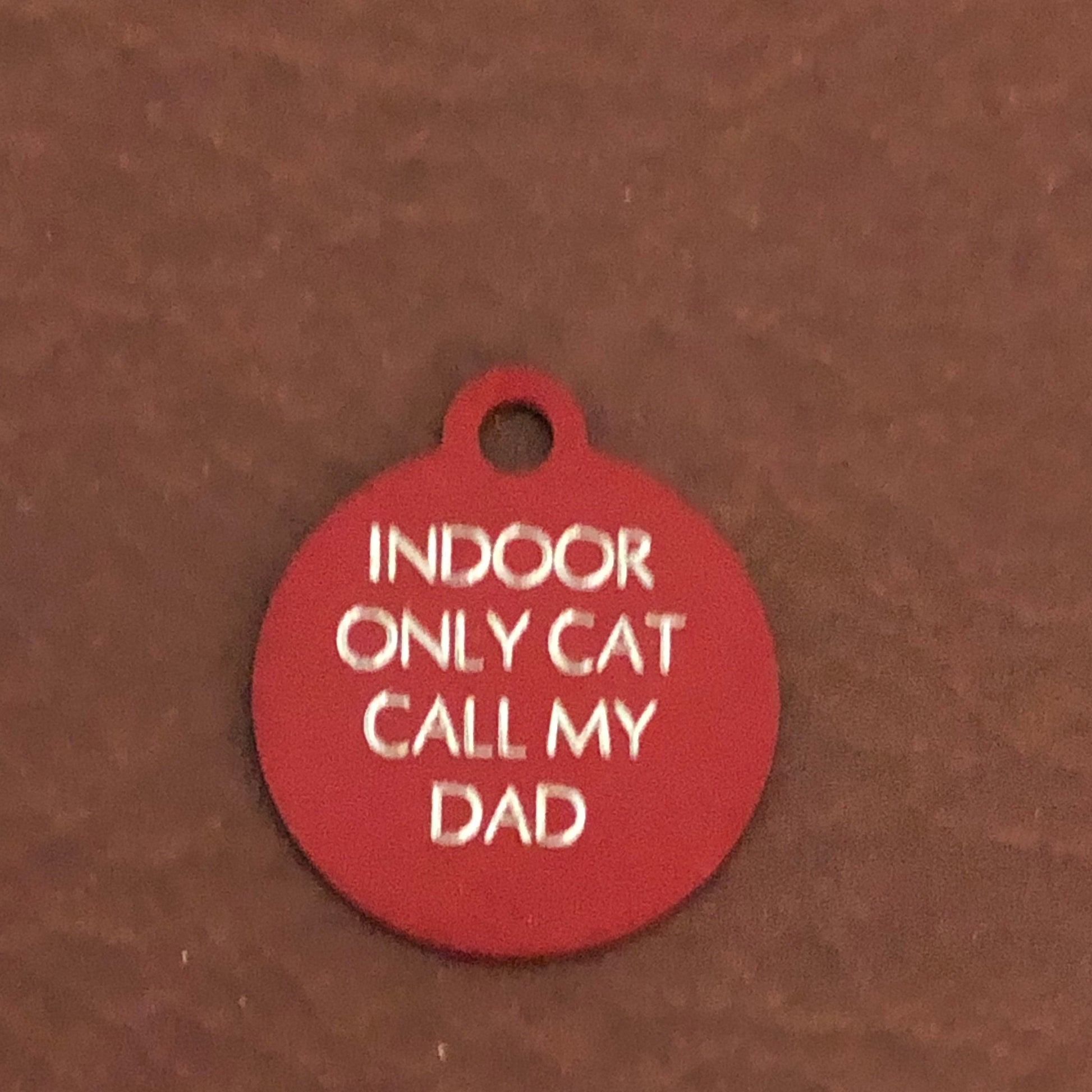 Small red circle tag that says: Indoor only cat call my dad. All engraved in capital letters.